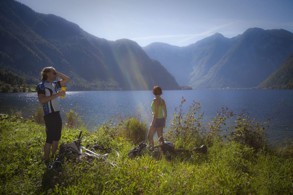 Bikewoche - Berge & Seen Twee fietsers pauzeren bij een meer met bergen op de achtergrond