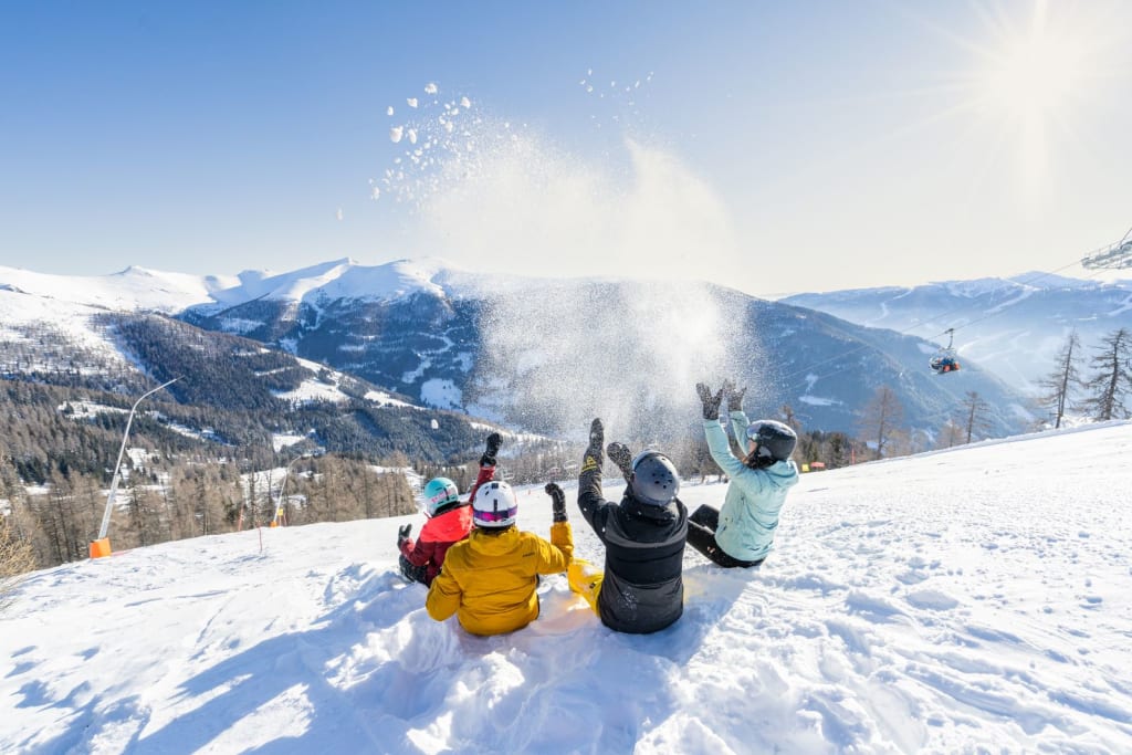 Vier Personen spielen im Schnee mit Bergen und klarem Himmel im Hintergrund