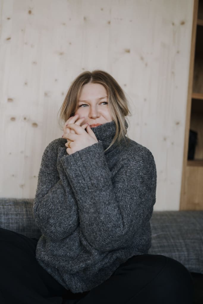 Woman in gray sweater warming hands and smiling while sitting