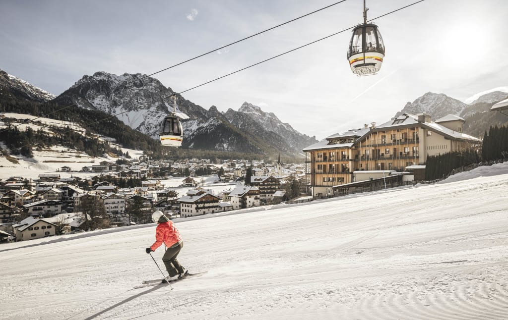 Skier on slope near cable cars and village with mountains in background