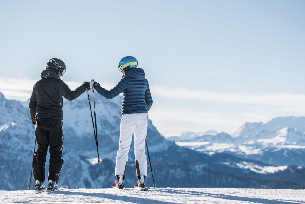 Two skiers fist bumping on snowy mountain peak with alpine landscape