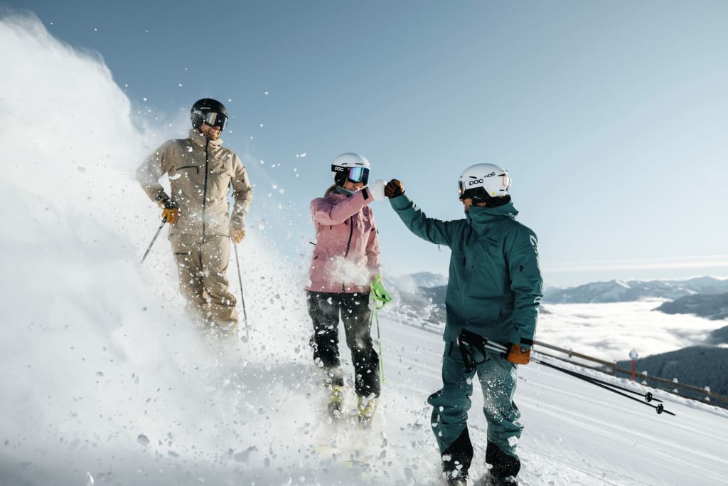 Three skiers in winter gear celebrating on a snowy mountain slope