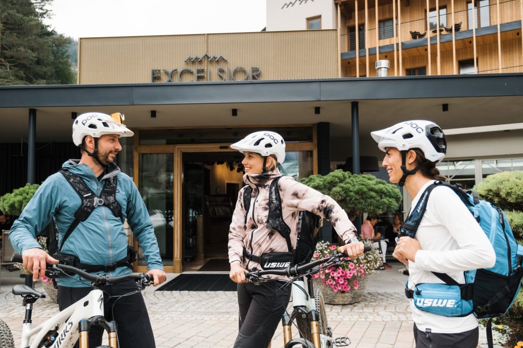 Three cyclists talking with helmets in front of a hotel