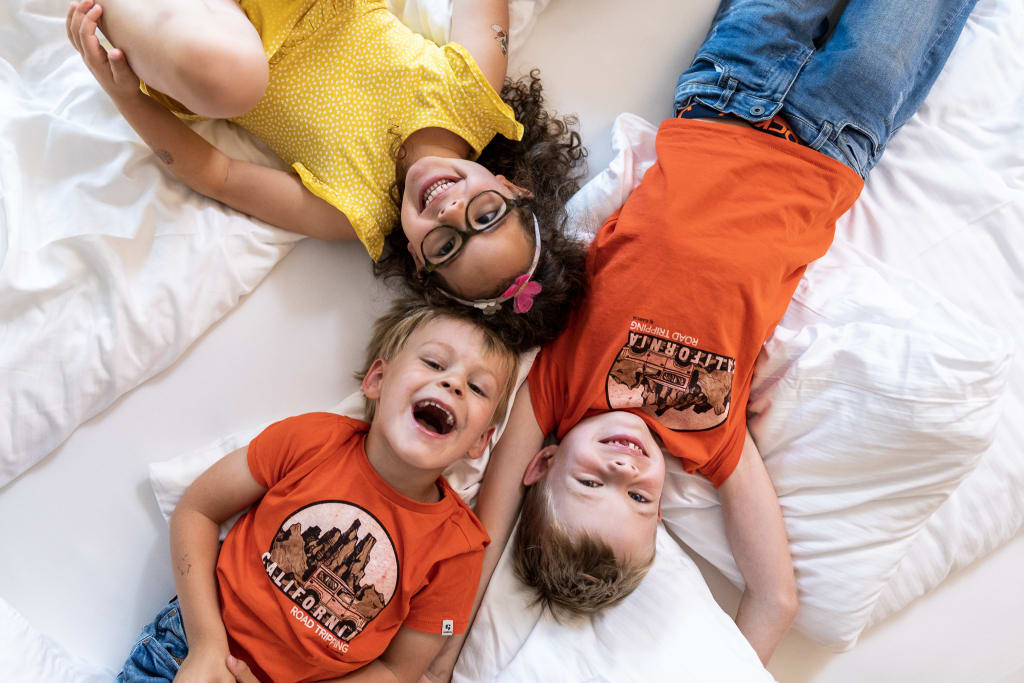 Three smiling children lying side by side on a bed