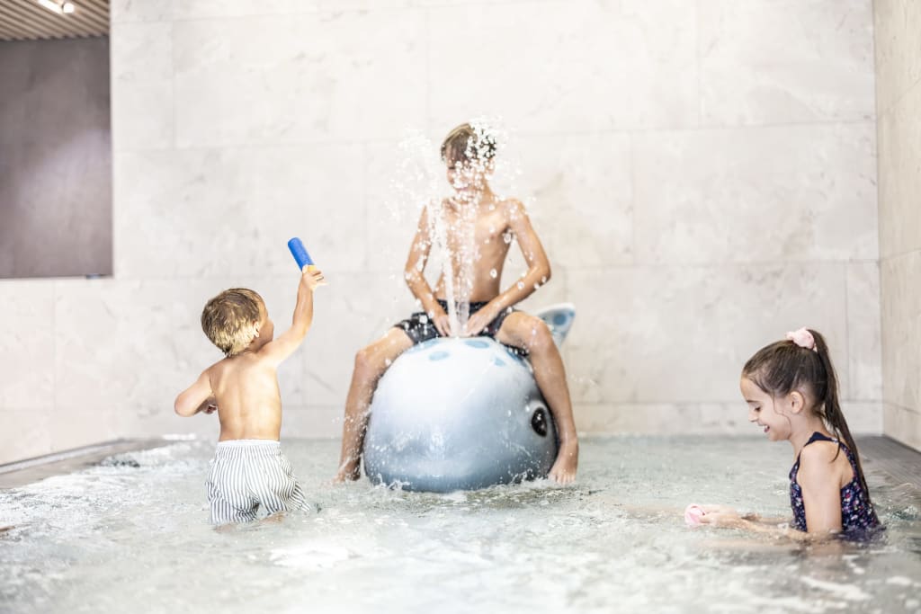 Three children playing in water, one sitting on a dolphin water spray toy.