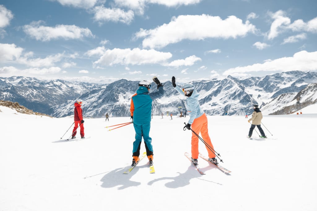 Two skiers highfiving on snowy slope with mountain background