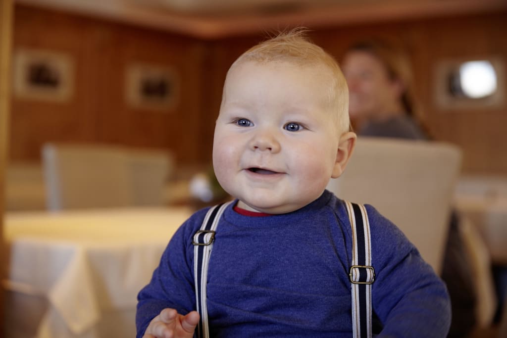 Lachende baby met blond haar en blauwe ogen in blauwe trui met bretels