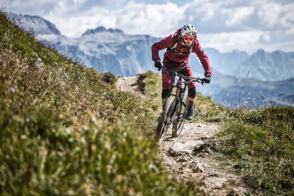 Bike Pauschale - kurz Aufenthalt 3 - 5 Mountainbiker in roter Kleidung fährt auf einem Bergpfad mit Alpen im Hintergrund