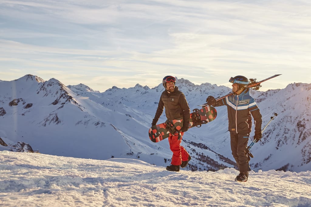 Two skiers and snowboarder hiking in snow with mountain backdrop at sunset