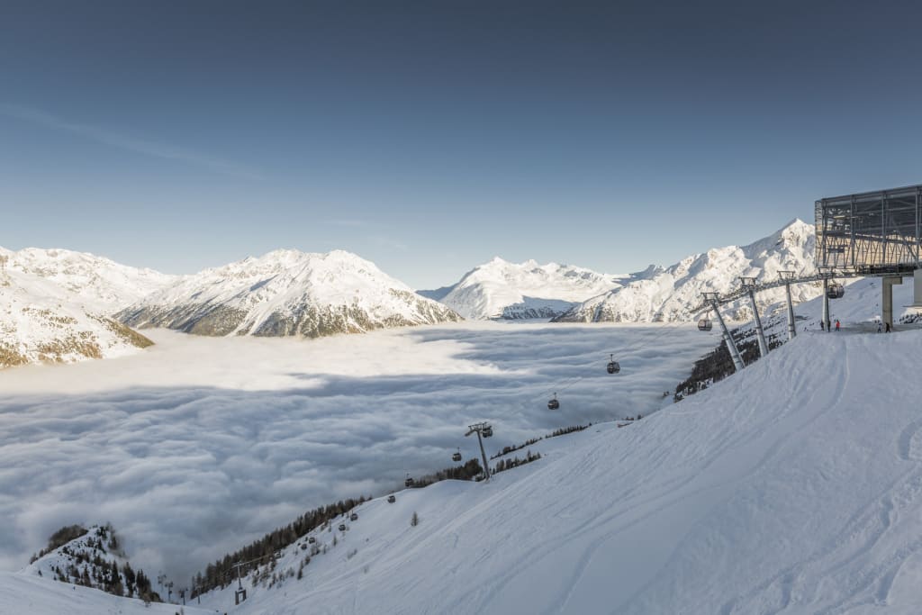 Snow-covered mountains with cable cars above a sea of fog under clear sky