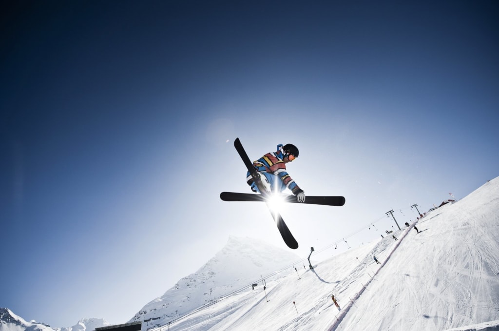 Skier performing a jump on a snowy slope under clear sky