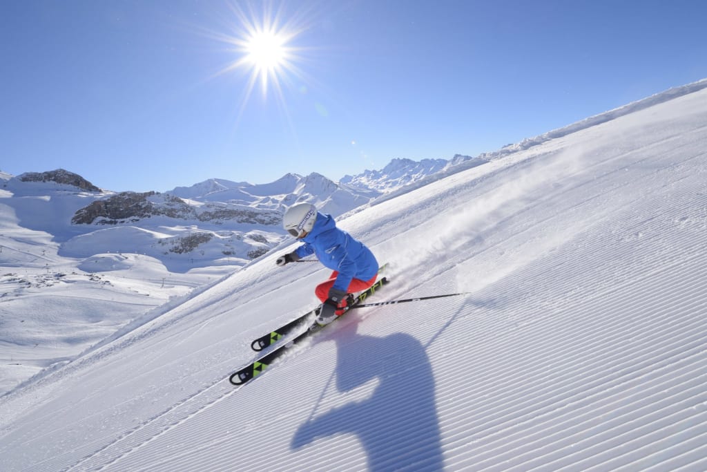 Person skiing down a groomed slope on a sunny day