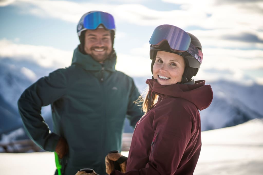 Smiling woman and man wearing ski goggles in winter clothing with snowy mountains