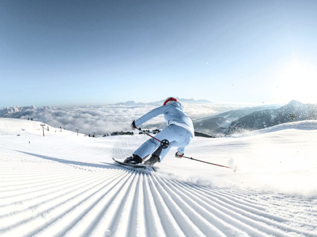 Skifahrer in weißer Kleidung fährt auf präparierter Skipiste bei klarem Himmel