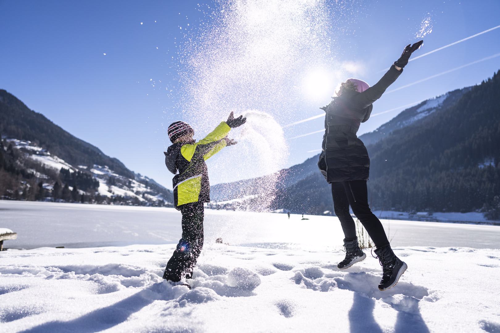 Kind und Frau spielen im Schnee vor Berglandschaft bei Sonnenschein